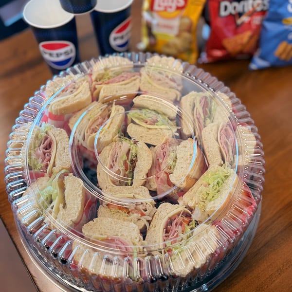 A catering platter of sandwiches with Pepsi cups and chip bags in the background.